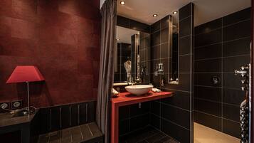 Un baño moderno con un tocador rojo, un espejo grande y baldosas oscuras.