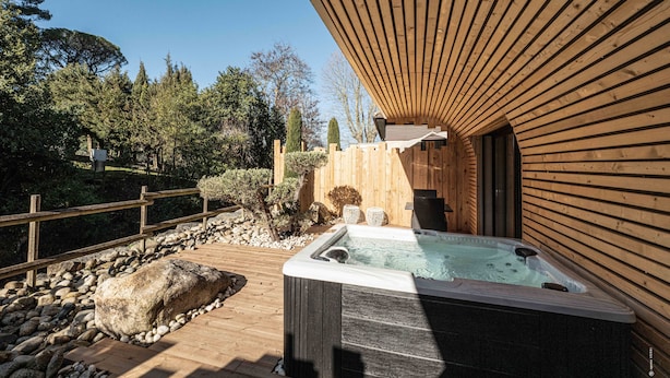 A wooden deck with a hot tub, surrounded by a wooden fence and a stone pathway.