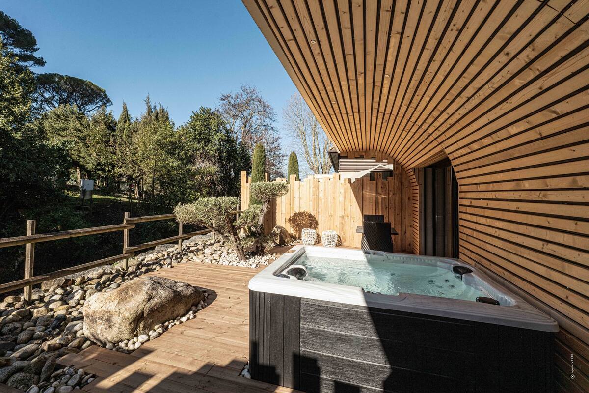 Una terraza de madera con un jacuzzi, rodeada por una valla de madera y un sendero de piedra.