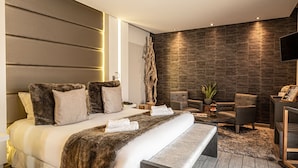 A modern bedroom with a large bed, a flat-screen TV, and a stone wall.