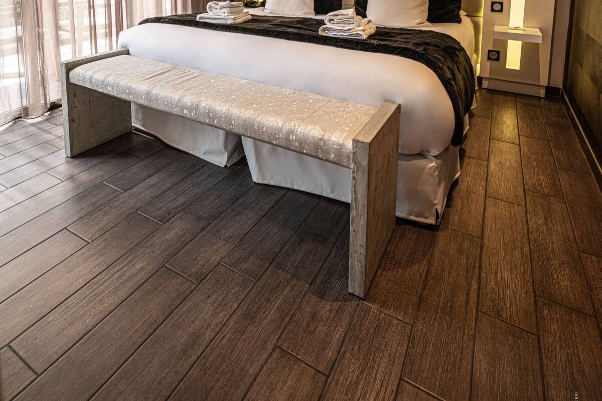 Un dormitorio de hotel moderno con una cama grande, un banco y una mesita de noche.