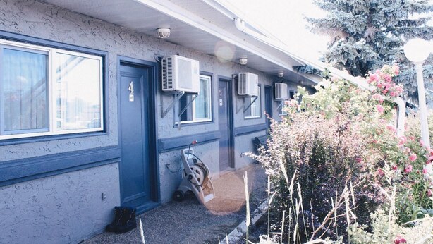 A building with a blue exterior, numbered door, and multiple air conditioning units. - Stardust Motel (Camrose)