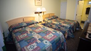 A hotel room with two beds, each with a colorful quilt, a bedside table with lamps, and a framed picture on the wall. - Stardust Motel (Camrose)