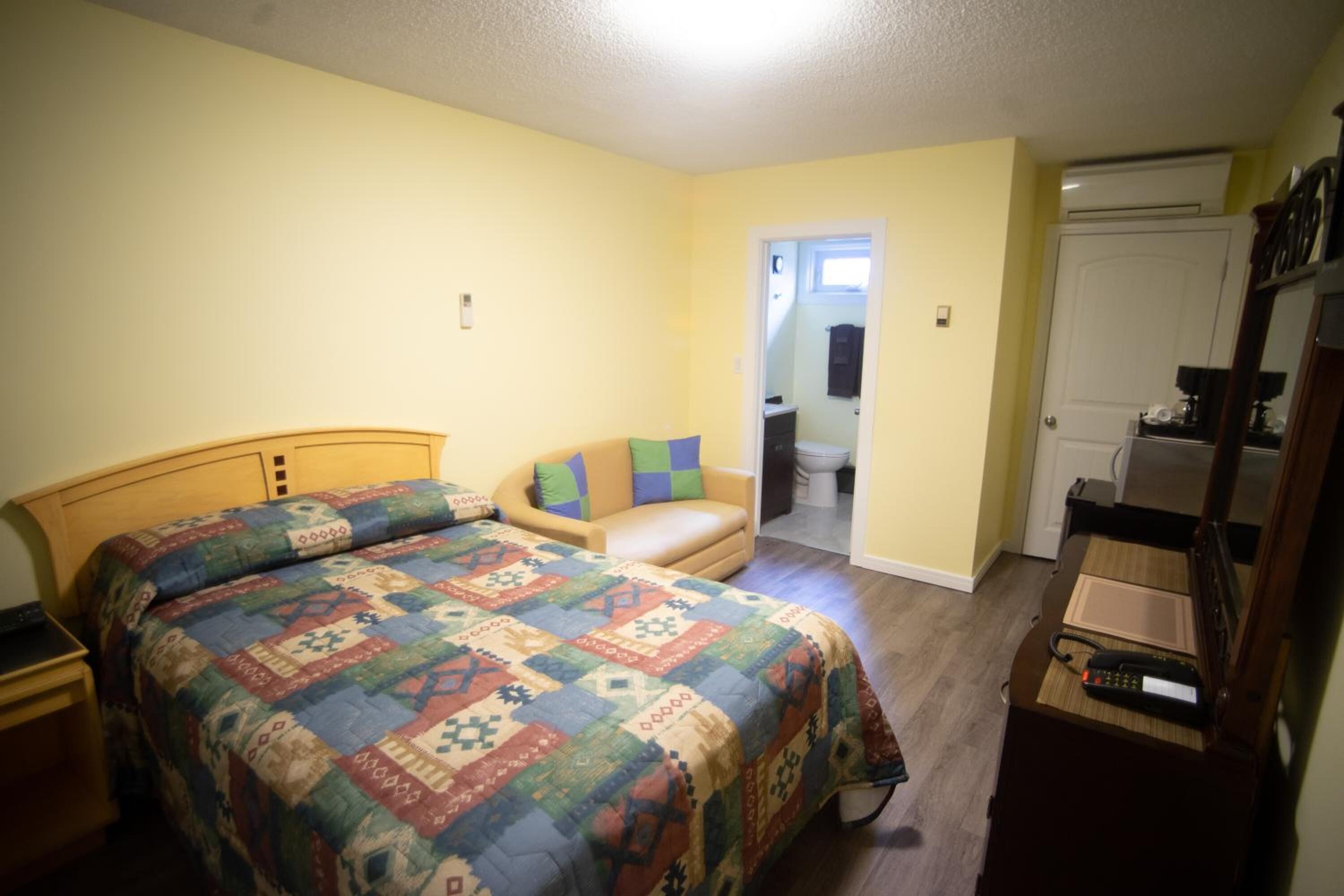 A bedroom with a bed, a chair, a desk, and a door leading to a bathroom.