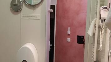 A bathroom with a white sink, a mirror, a toilet paper dispenser, a trash bin, and a towel hanging on the wall.