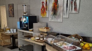 A modern kitchen with a coffee machine, a buffet table with food items, and artwork on the wall.
