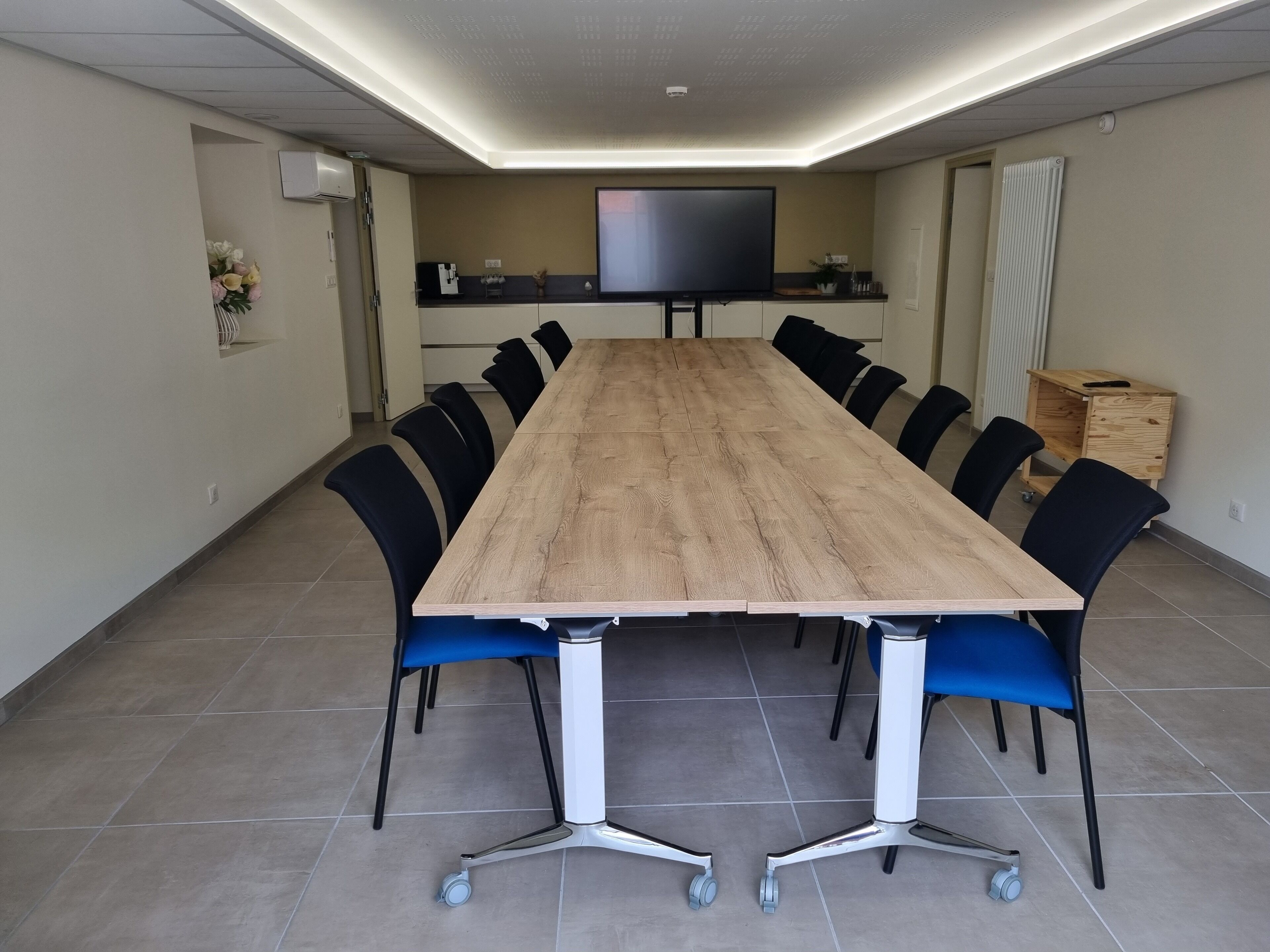 A conference room with a long table, black chairs, and a flat-screen TV.