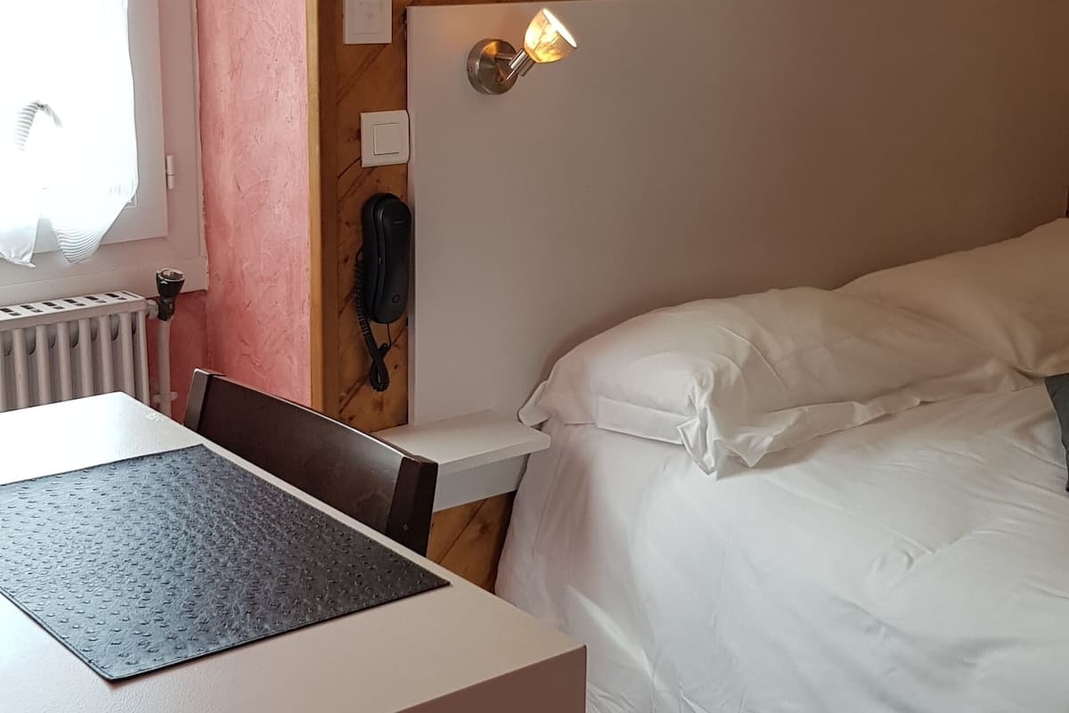 Une chambre avec un plafond en bois, un lit avec une literie blanche, un bureau avec une chaise et deux lampes fixées au mur.