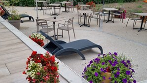 An outdoor patio area with tables and chairs, surrounded by potted plants and umbrellas.