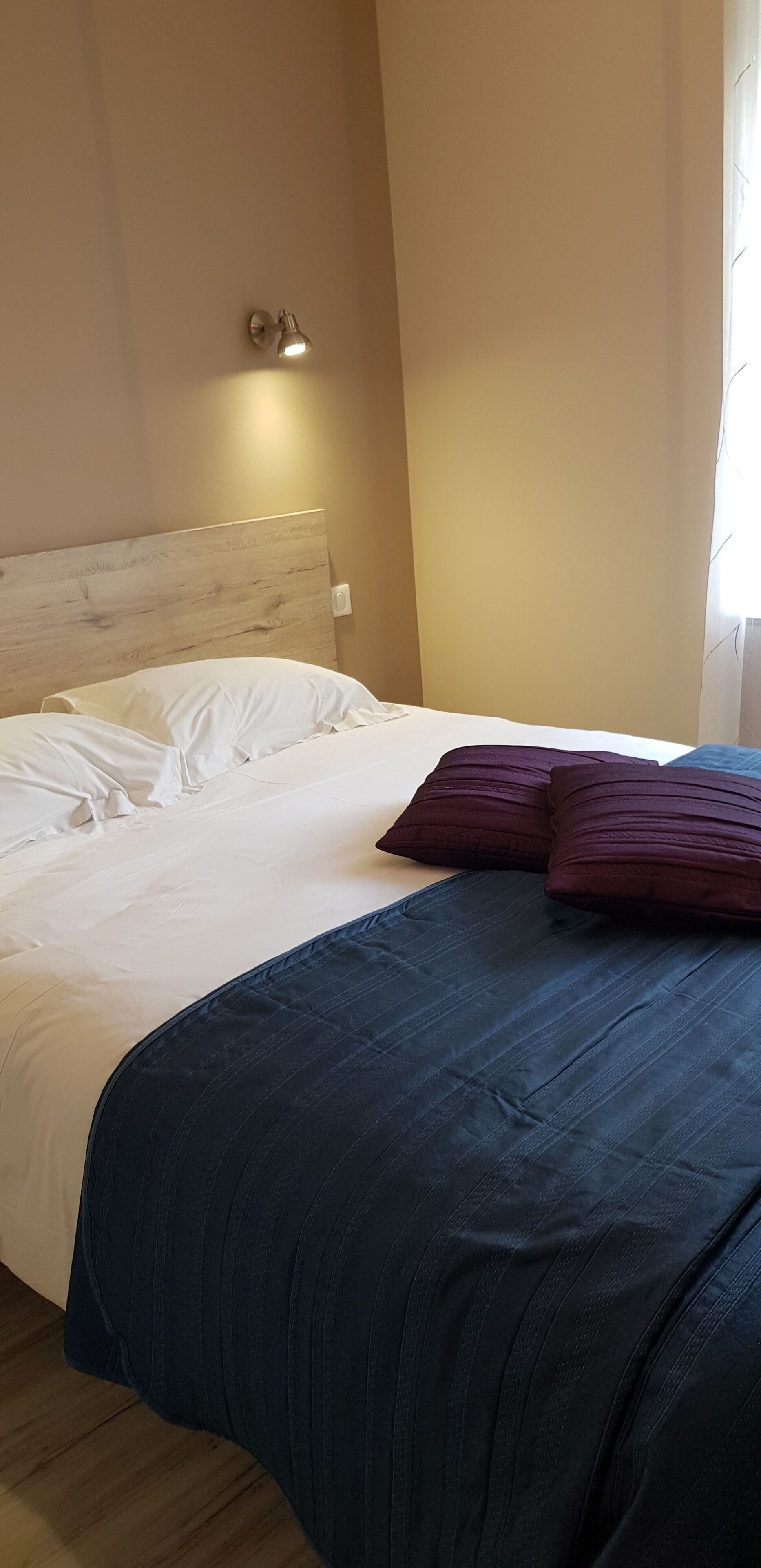 Un lit bien fait, avec une literie blanche et bleu foncé, une tête de lit et un luminaire fixé au mur.
