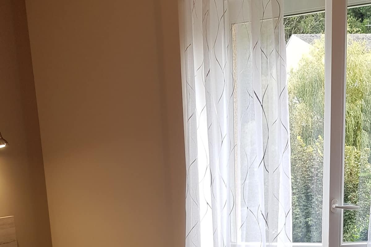 Une chambre à coucher avec un lit, une fenêtre avec des rideaux et une vue sur la verdure.