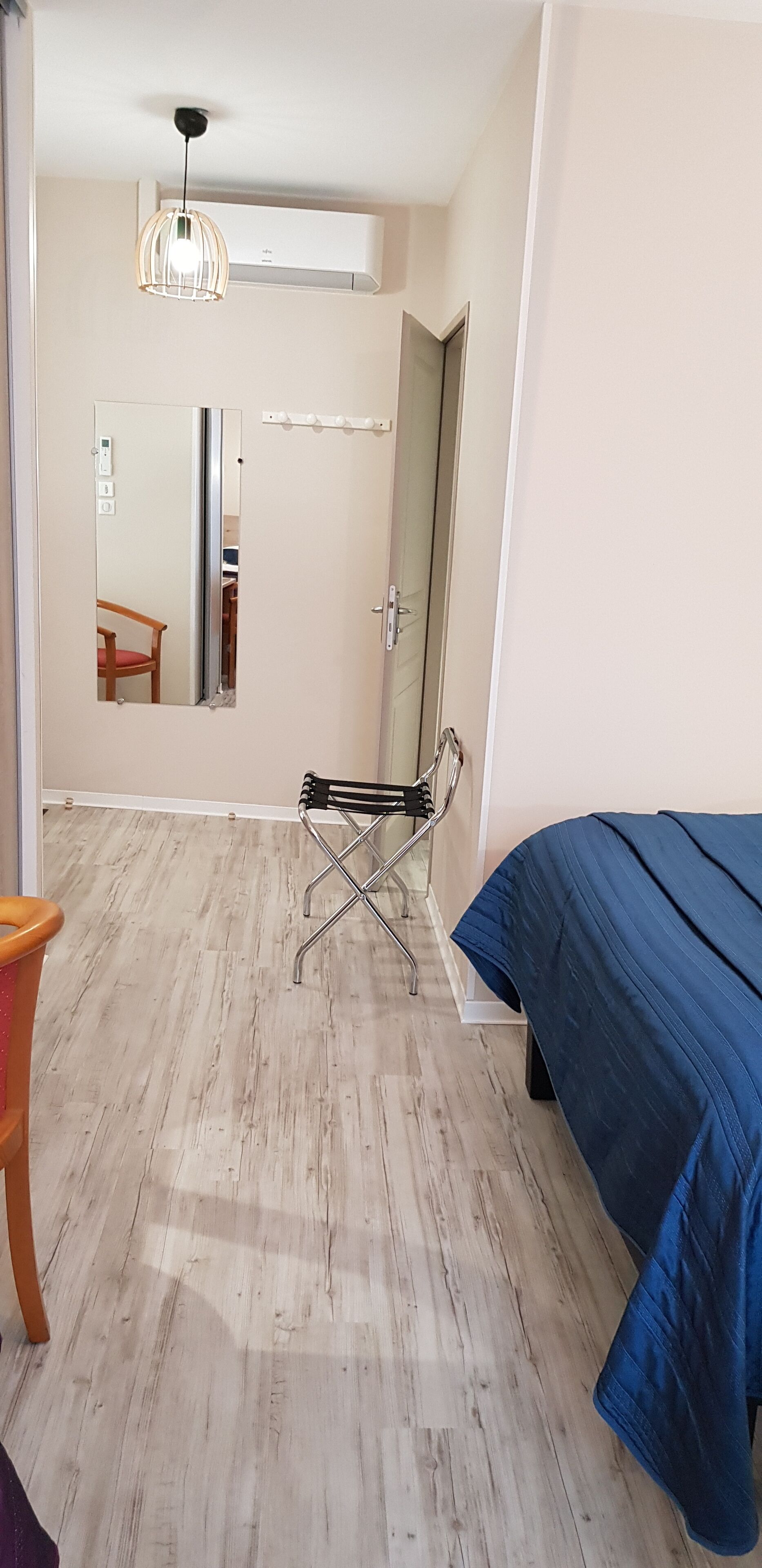 A bedroom with a bed, a chair, a mirror, and an air conditioning unit.