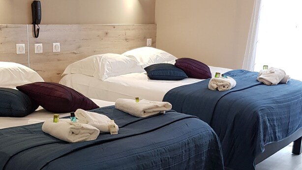 A hotel room with two beds, each with a blue bedspread and white linens. There are towels on the beds, and a phone on the headboard. The room has wooden flooring and a light-colored wall.
