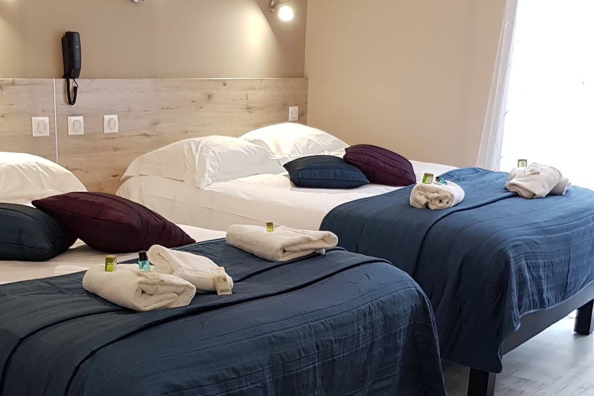Une chambre d’hôtel avec deux lits, chacun recouvert d’une couverture bleue et doté de draps blancs. Des serviettes sont posées sur les lits, et un téléphone se trouve sur la tête de lit. La chambre est dotée d’un plancher en bois et d’un mur de couleur claire.