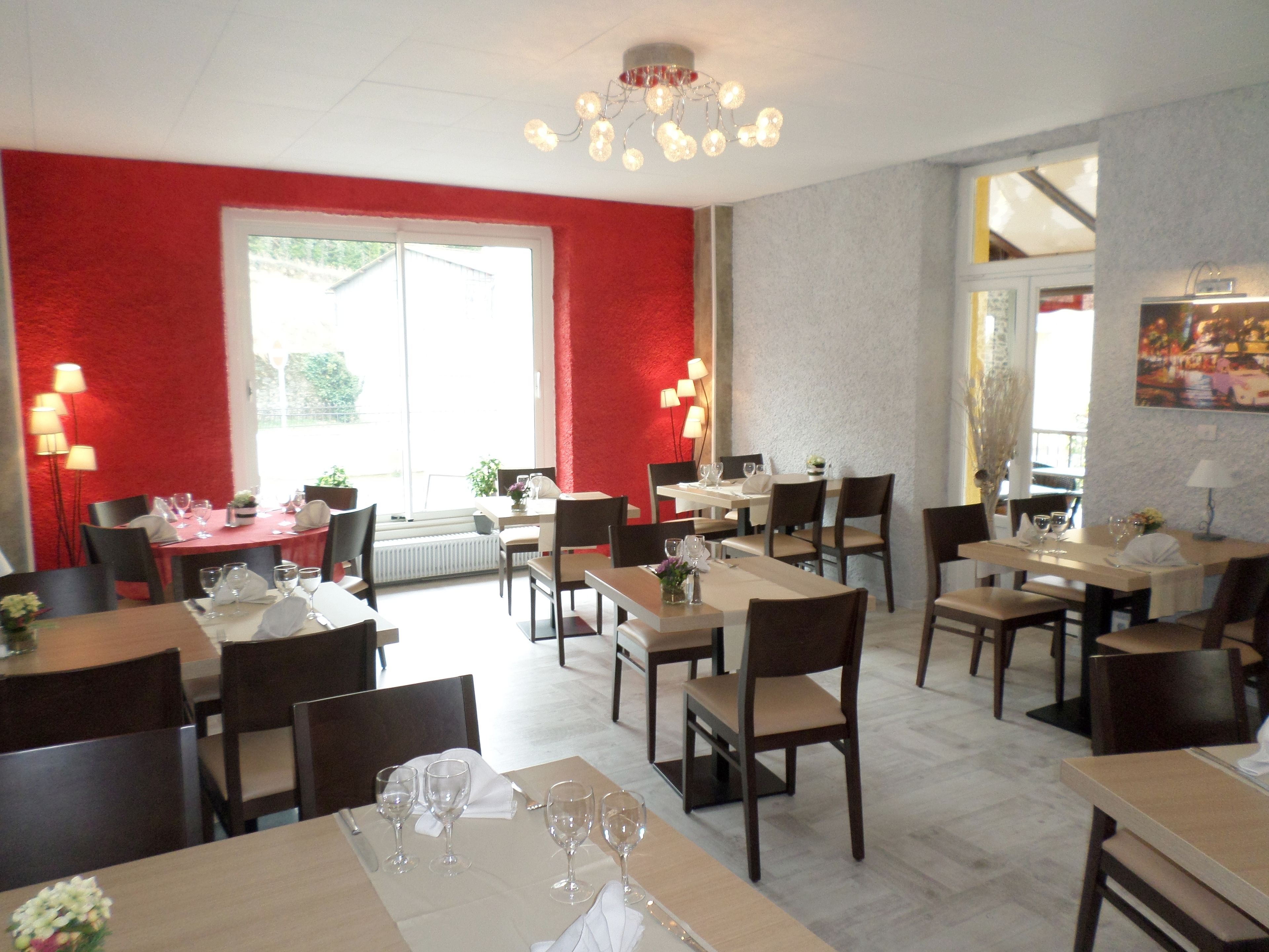 A restaurant with multiple tables and chairs, red walls, and a chandelier.