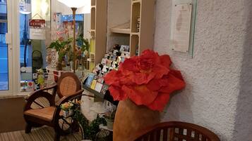 A cozy room with a wooden chair, a table with a vase of flowers, and a shelf with magazines and a lamp.