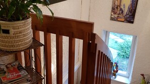 A room with a wooden staircase, a potted plant, a magazine rack, and a cityscape painting.