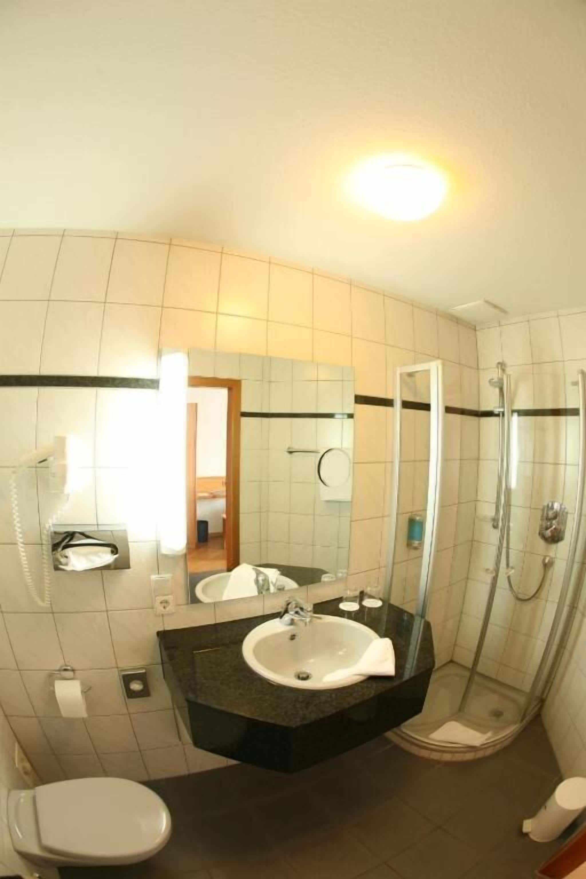 A bathroom with a toilet, sink, mirror, and shower.