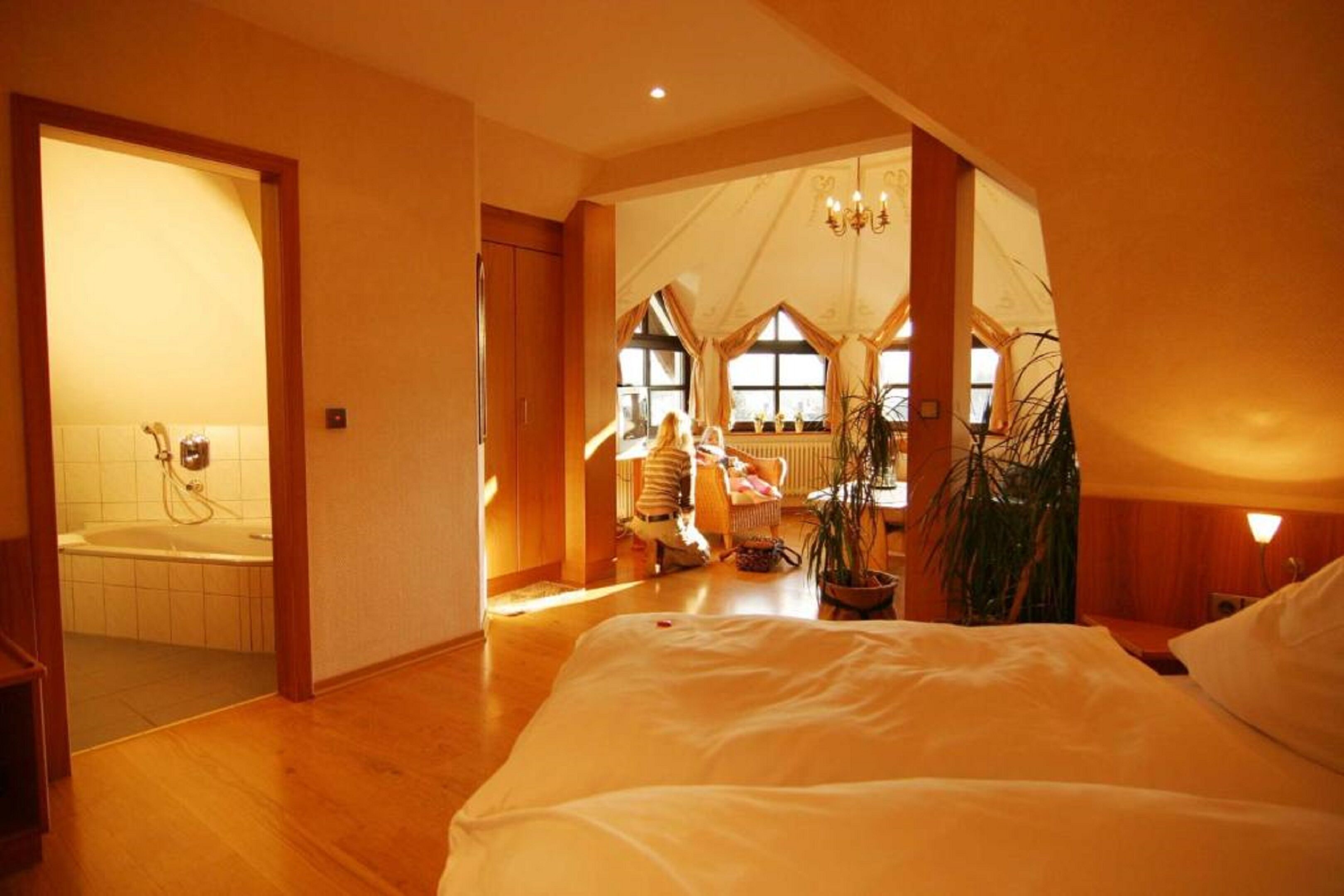 A spacious bedroom with a large bed, a visible bathroom with a bathtub, and a cozy sitting area with a child playing.