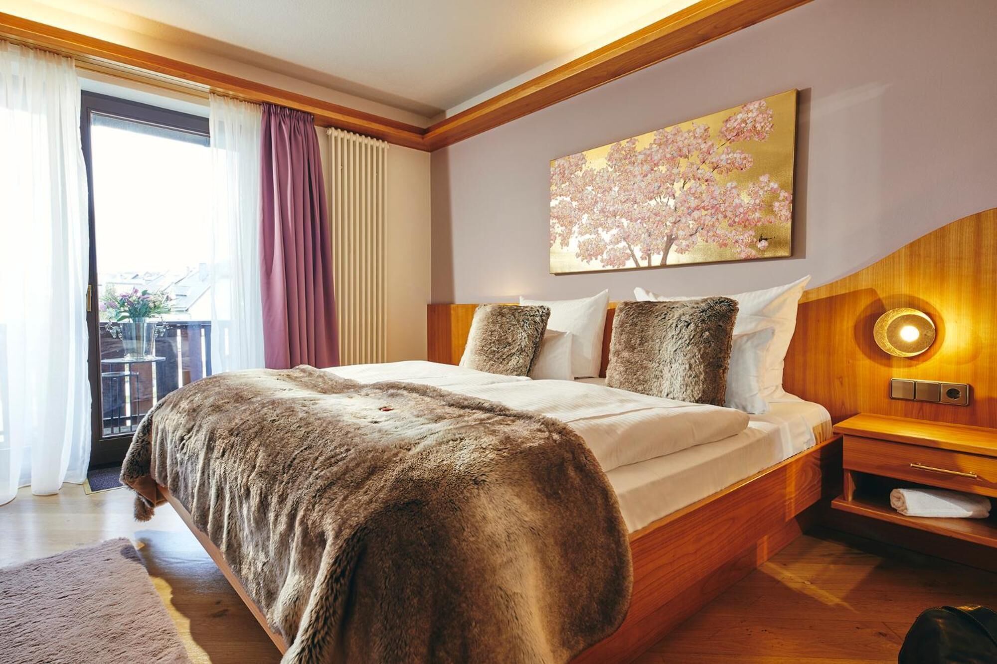 A bedroom with a large bed, wooden headboard, a nightstand, and a painting of cherry blossoms.