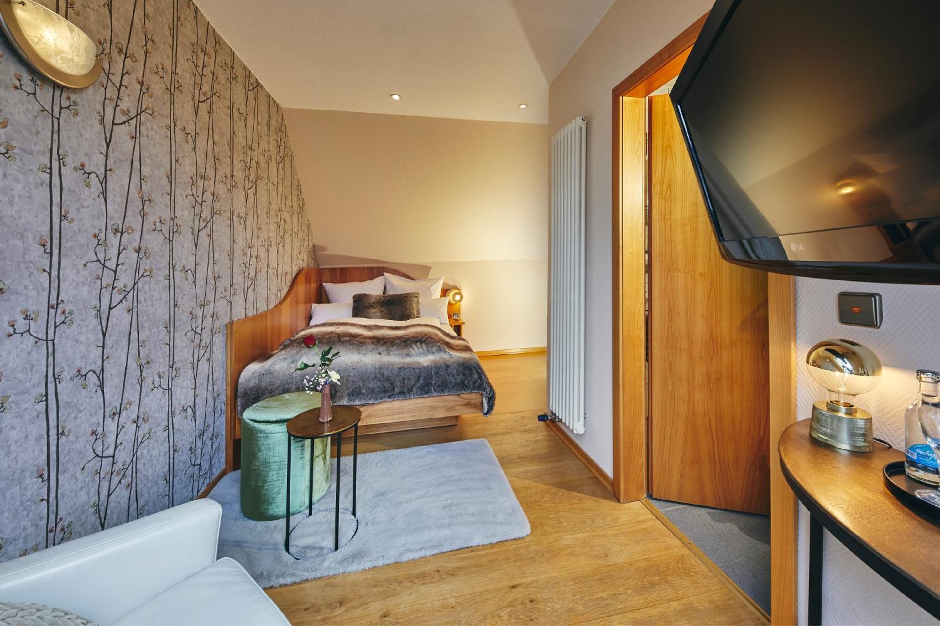 Une chambre d’hôtel moderne avec un lit en bois, une télévision, une petite table d’appoint et un radiateur.
