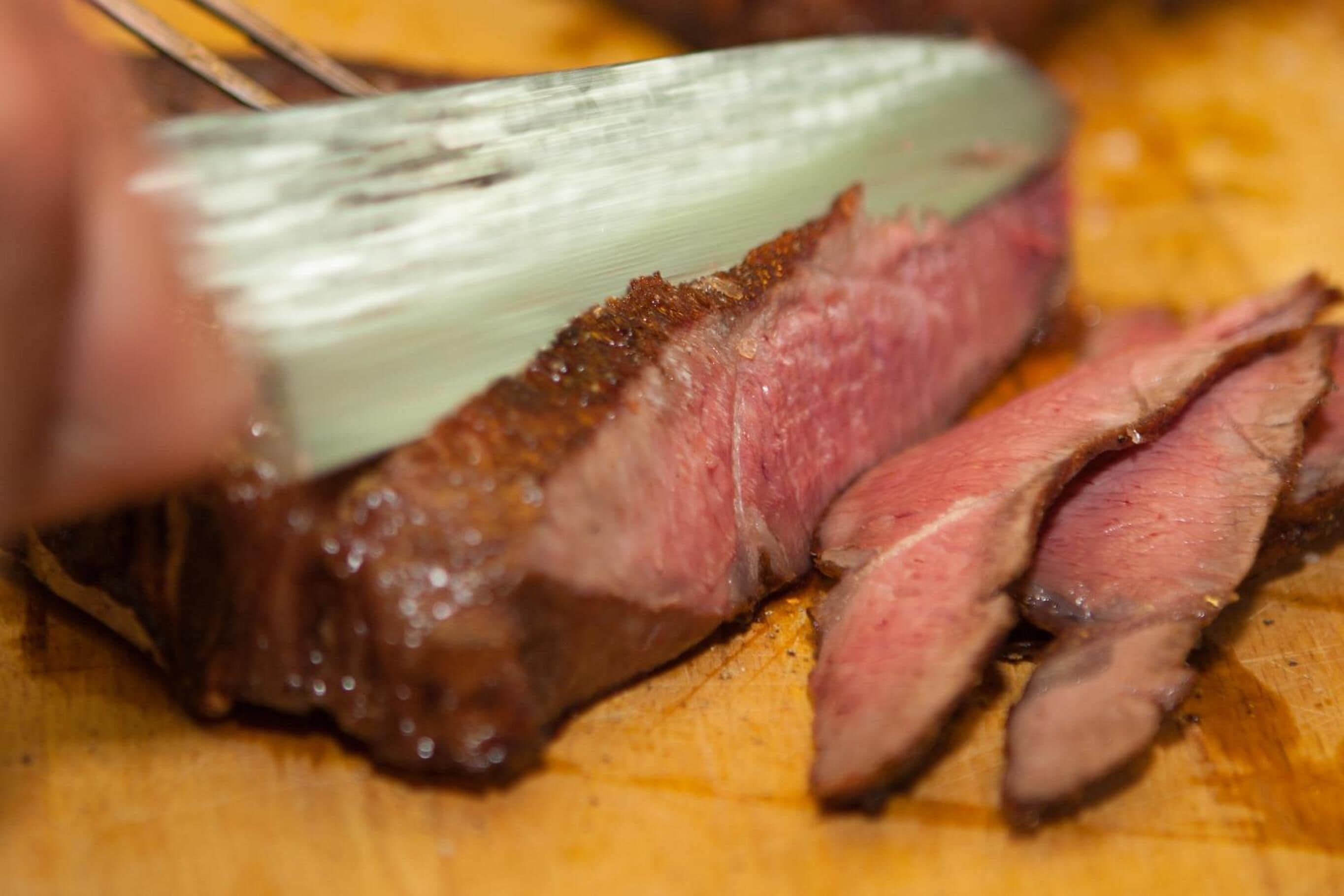 A close-up of a steak being sliced on a wooden cutting board.
