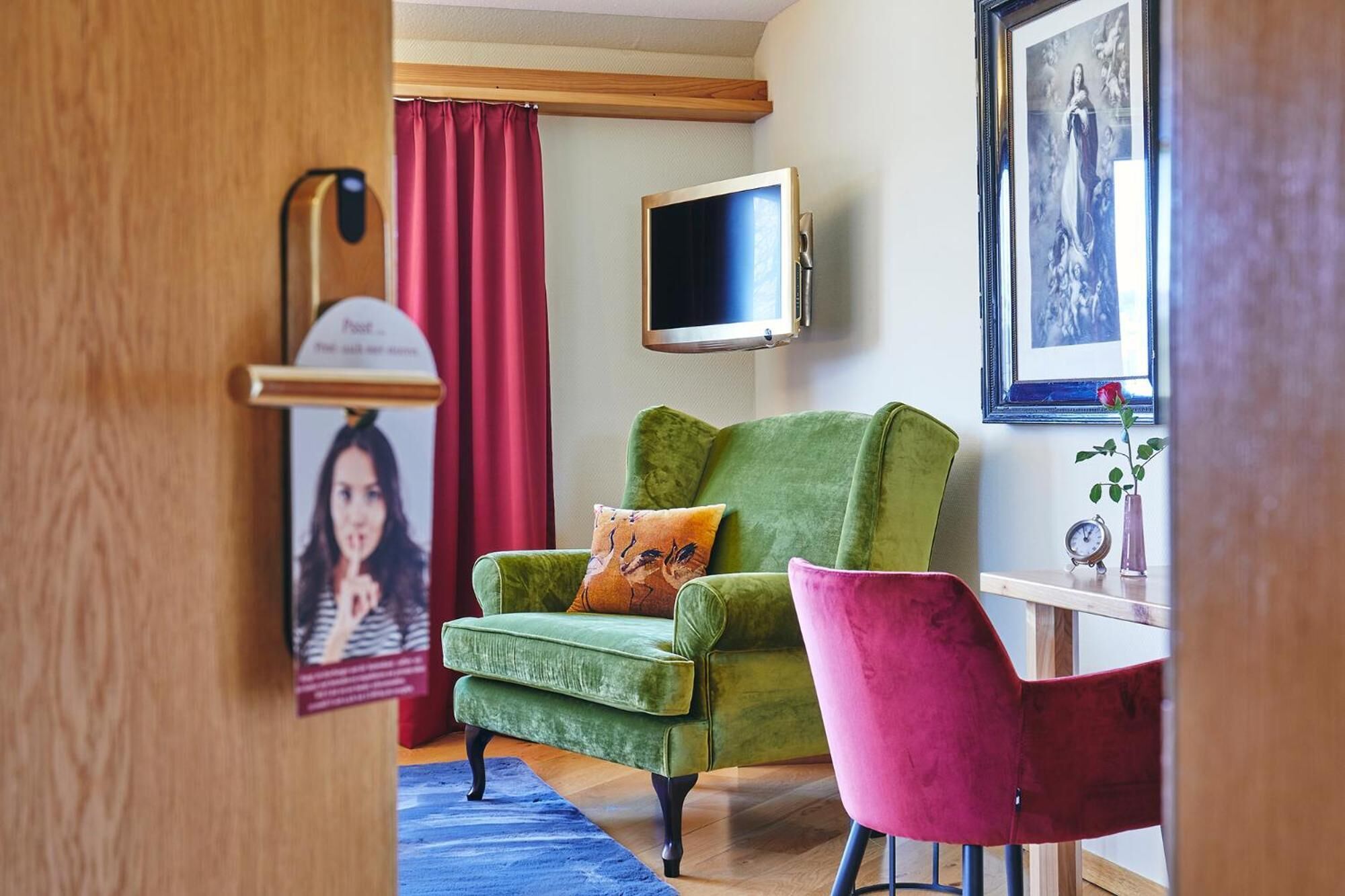A room with a green armchair, a pink chair, a flat-screen TV, and a framed picture on the wall.