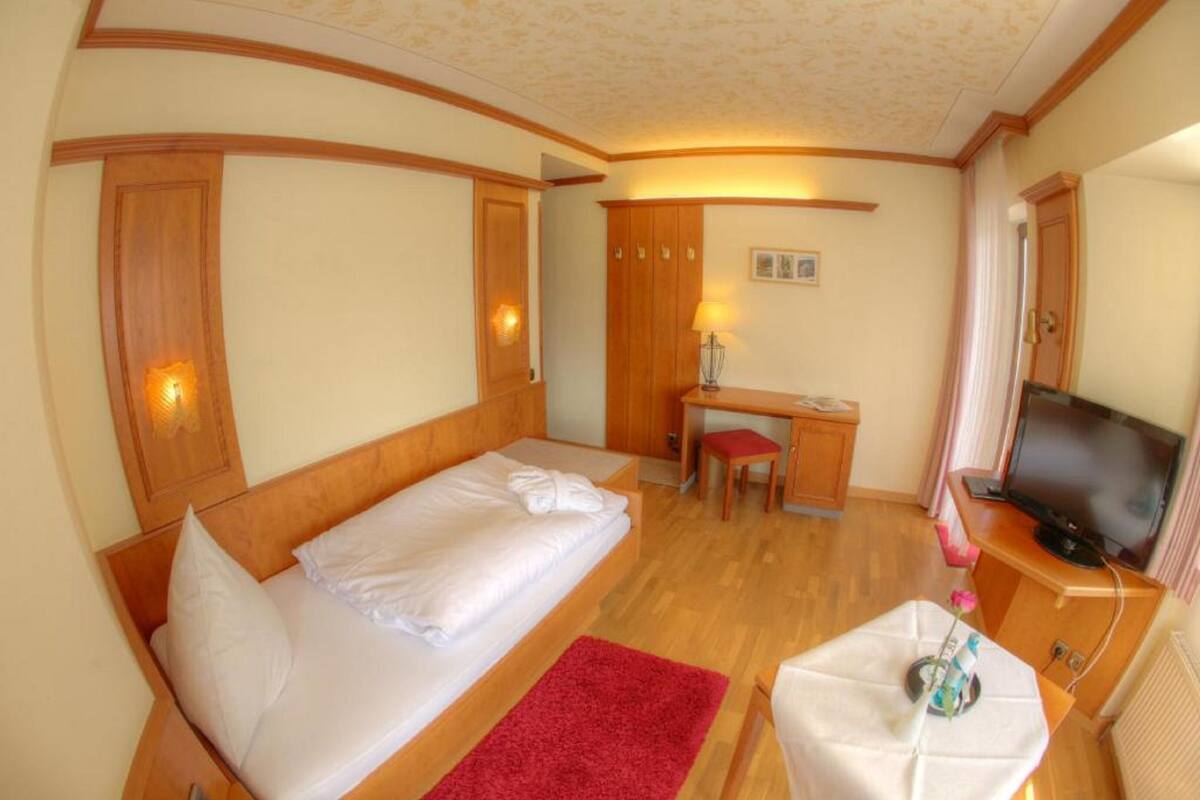 Une chambre d’hôtel avec un lit, un bureau, une télévision et une petite table surmontée d’un tapis rouge.
