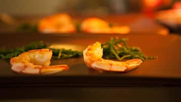 A plate with two shrimp and some greens on a dark surface.
