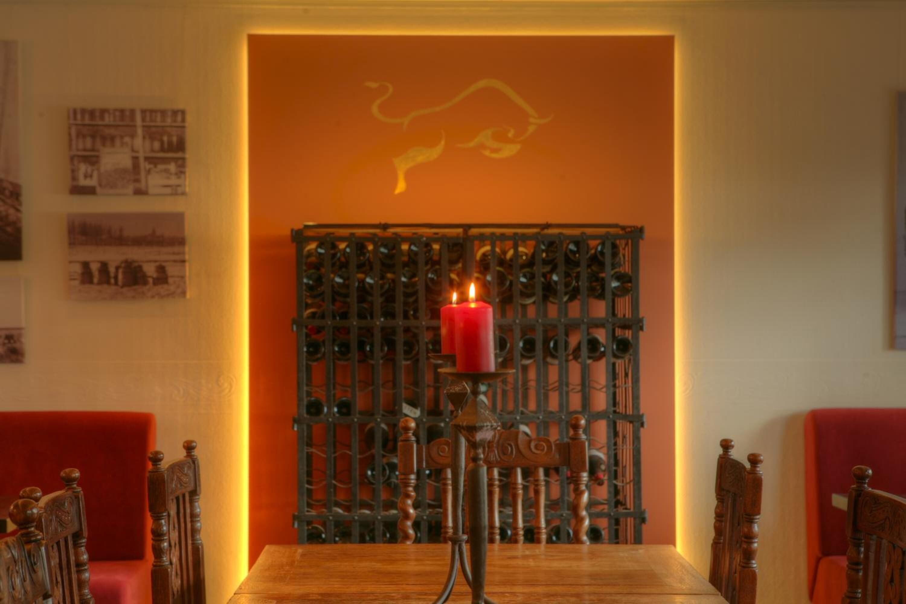 A dining area with a wooden table, red upholstered chairs, a candle on a candelabra, and a decorative metal grille in the background.