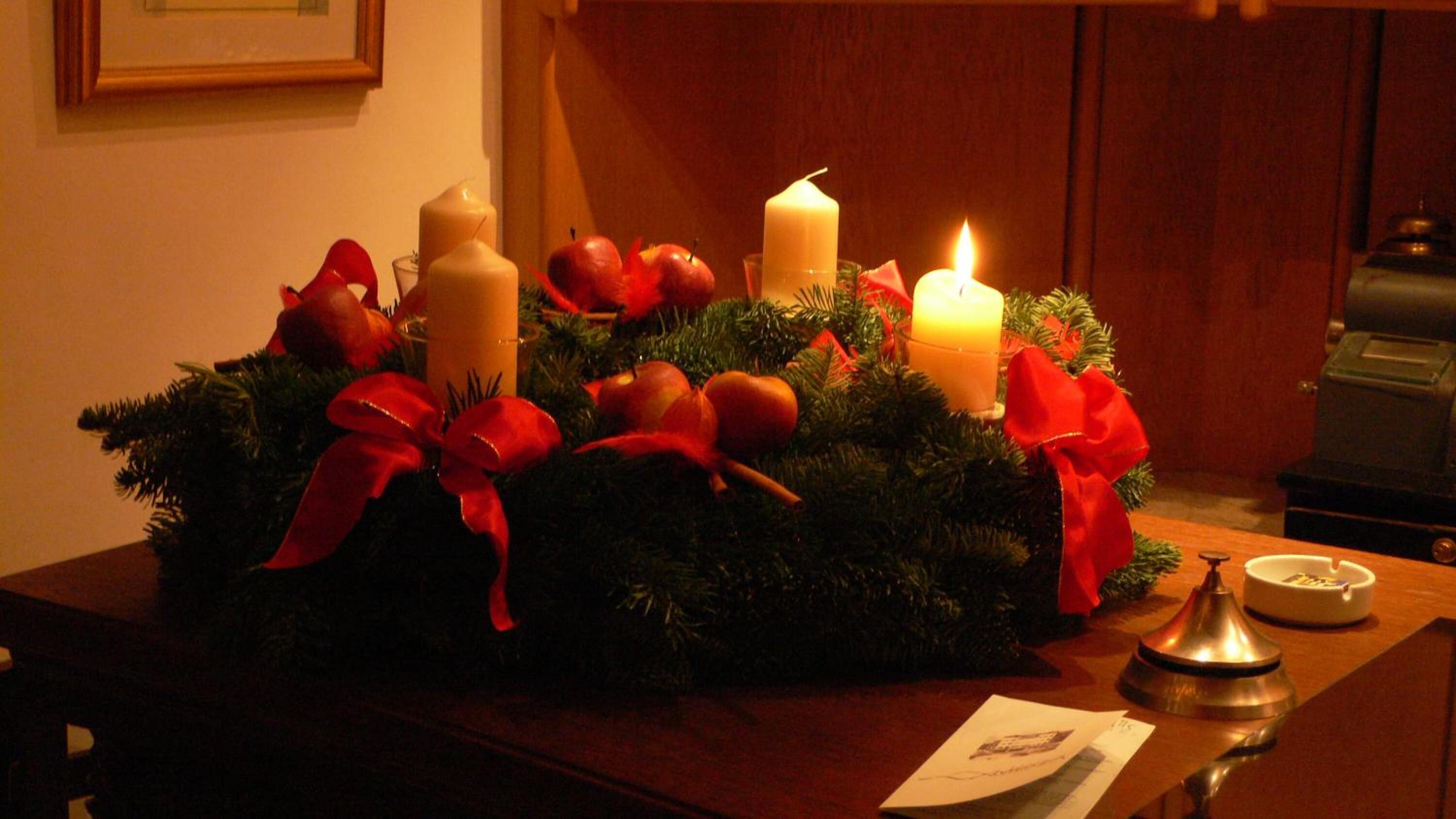 Una mesa con decoración navideña que incluye velas, manzanas rojas y un lazo rojo.