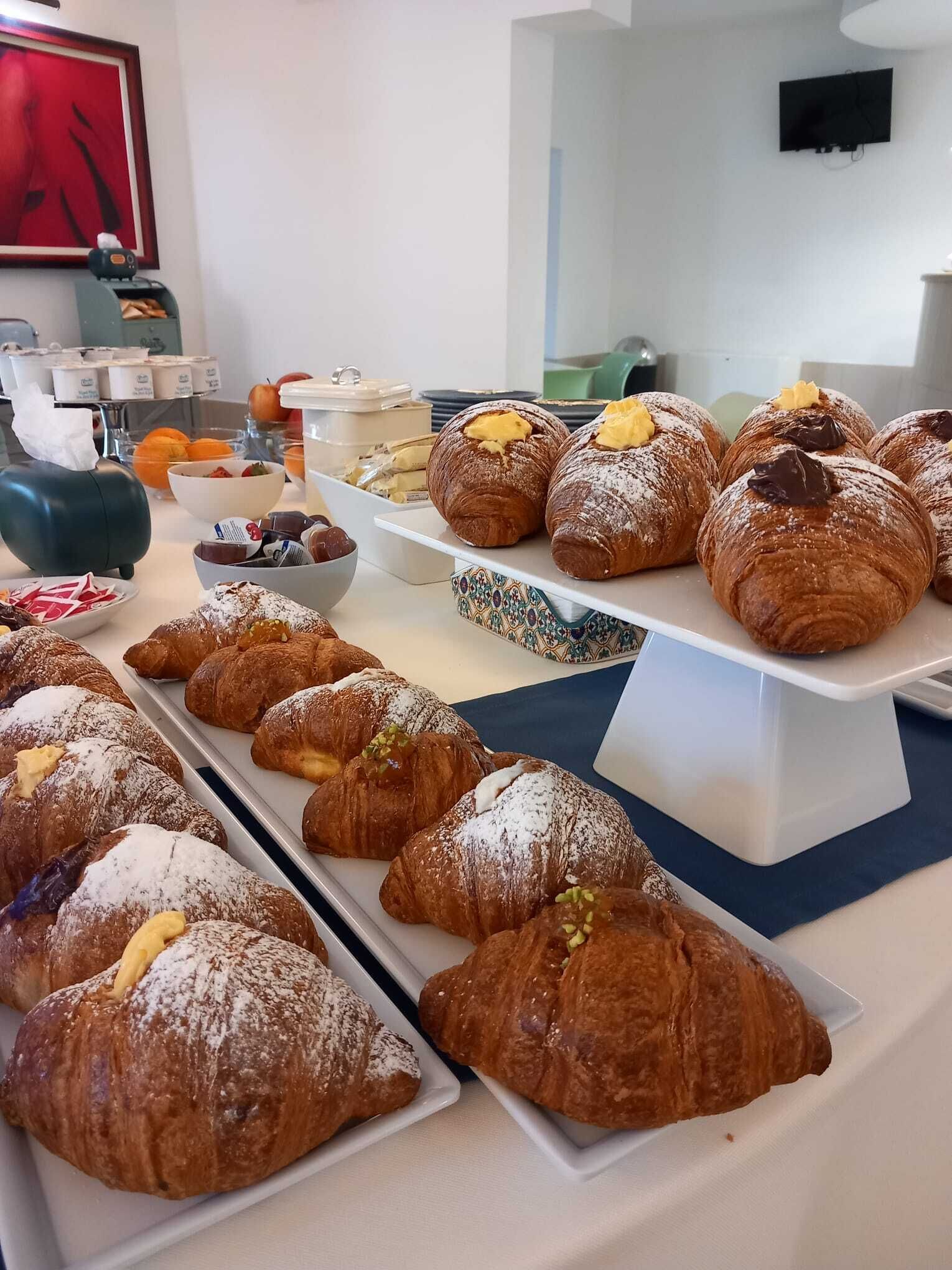 A buffet table with various pastries and desserts, including croissants and fruit bowls.