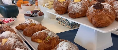 A buffet table with various pastries and desserts, including croissants and fruit bowls.