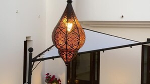 An outdoor area with a hanging decorative light fixture, a white wall, and a potted plant. - Hotel Villa Ionia (Avola)