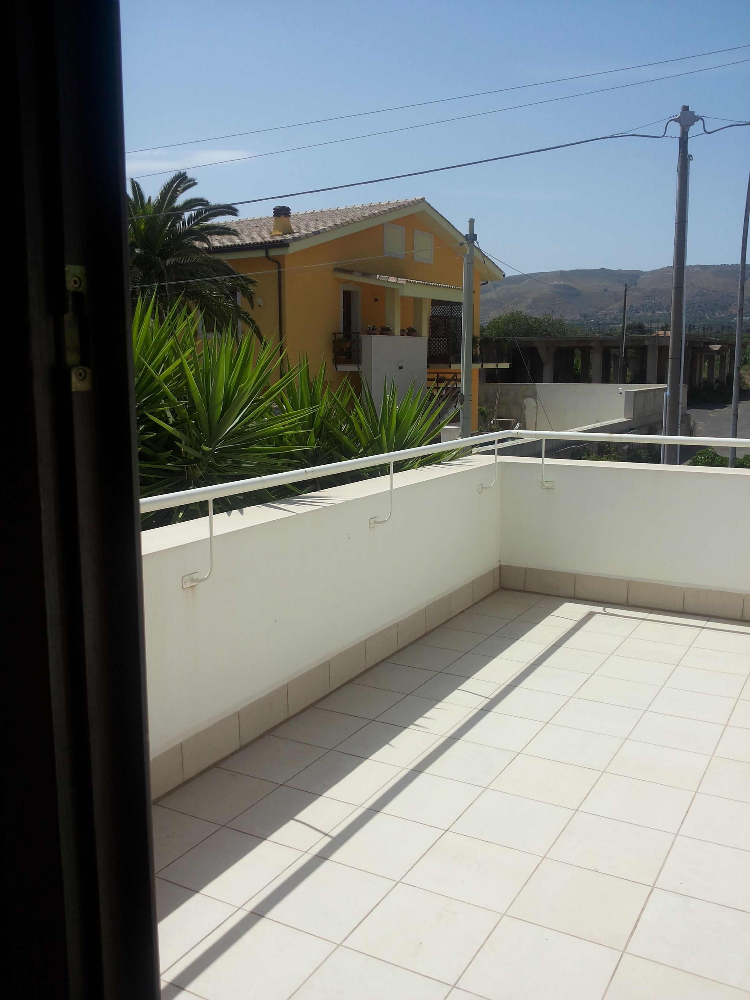 A balcony with a tiled floor, a white railing, and a view of a yellow building with a tiled roof.