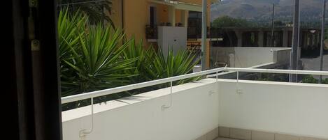 A balcony with a tiled floor, a white railing, and a view of a yellow building with a tiled roof.
