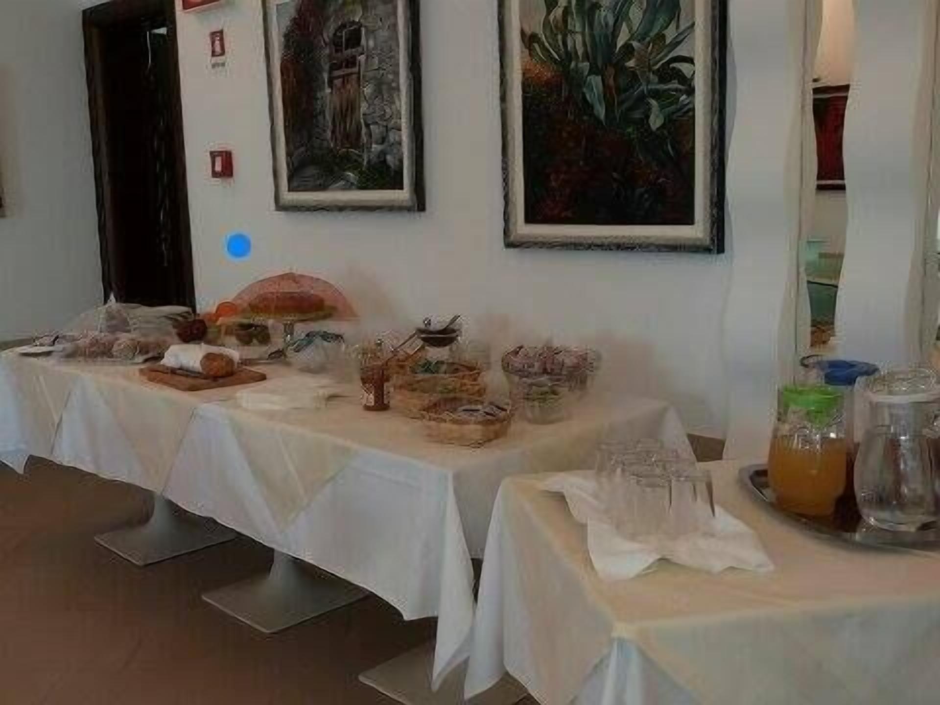 Un buffet est installé avec divers plats et boissons disposés sur des tables, le tout placé devant un mur orné d’œuvres d’art encadrées.