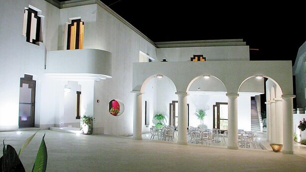 A modern building with a courtyard, featuring white walls, multiple arches, and a staircase leading to an upper level. - Hotel Villa Ionia (Avola)