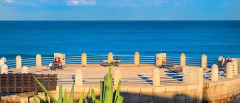 A waterfront promenade with benches and a railing overlooking the sea.