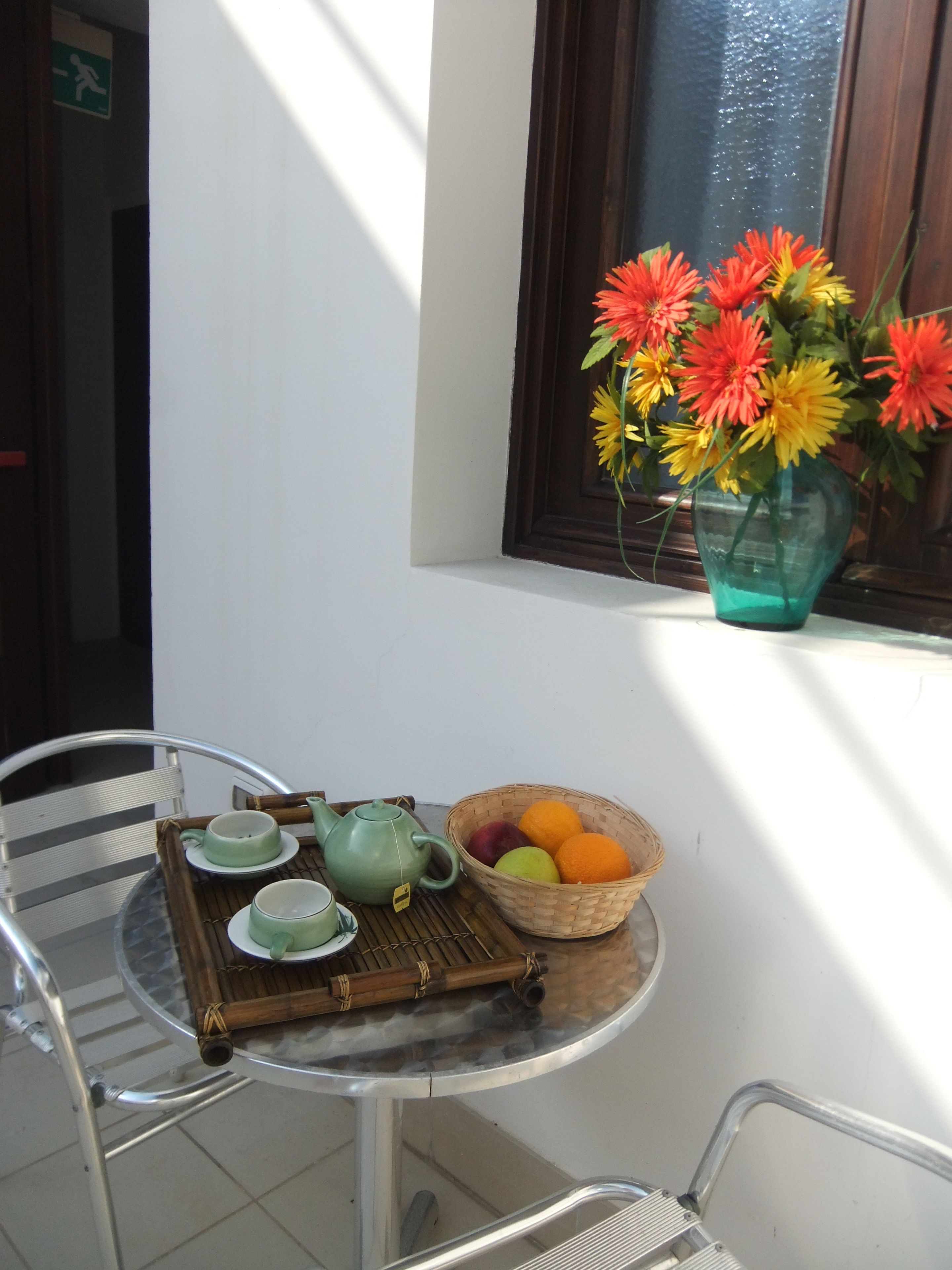 A small round table with a green teapot, cups, and a basket of fruit.