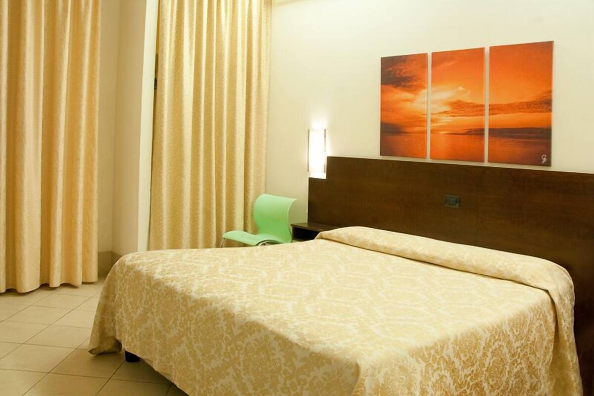 Hotellihuone, jossa on sänky, tuoli ja seinälle asennettu televisio.