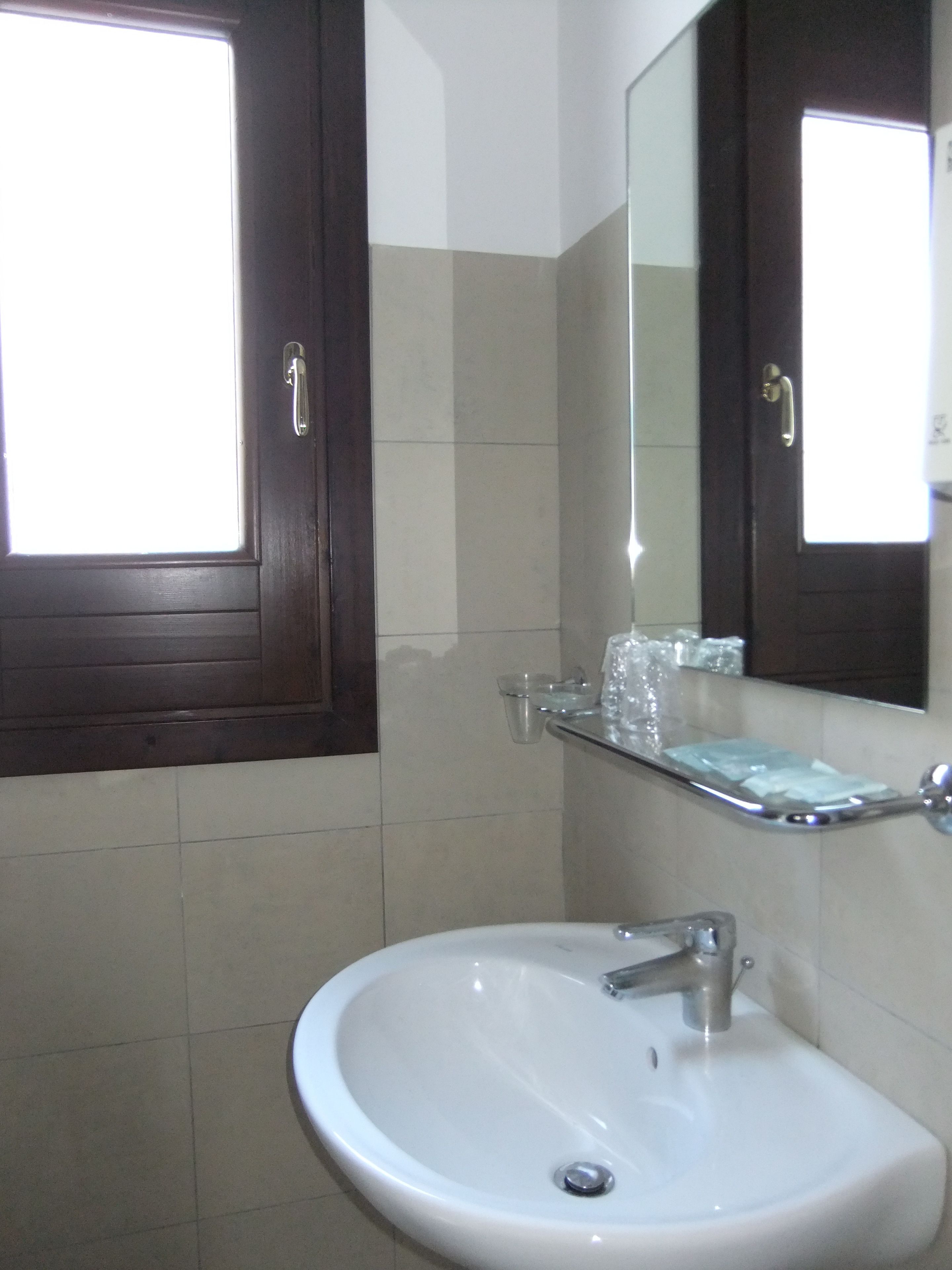 A bathroom with a white sink, a mirror, and a window with a wooden door.
