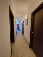 Un estrecho pasillo con suelo de baldosas, puertas de madera y cuadros en las paredes.
