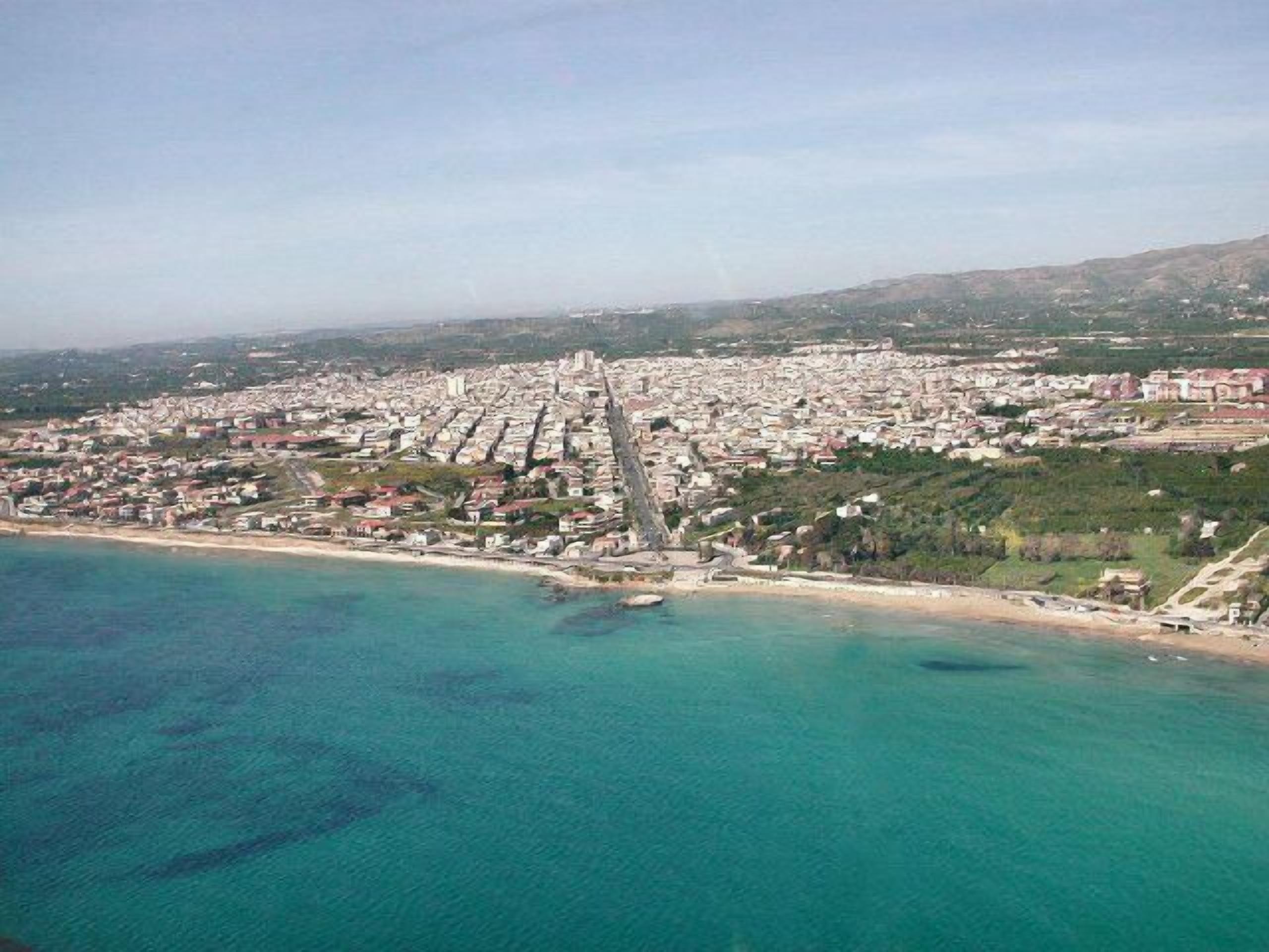 An aerial view of a coastal city with a dense urban area, a prominent church, and a beach.