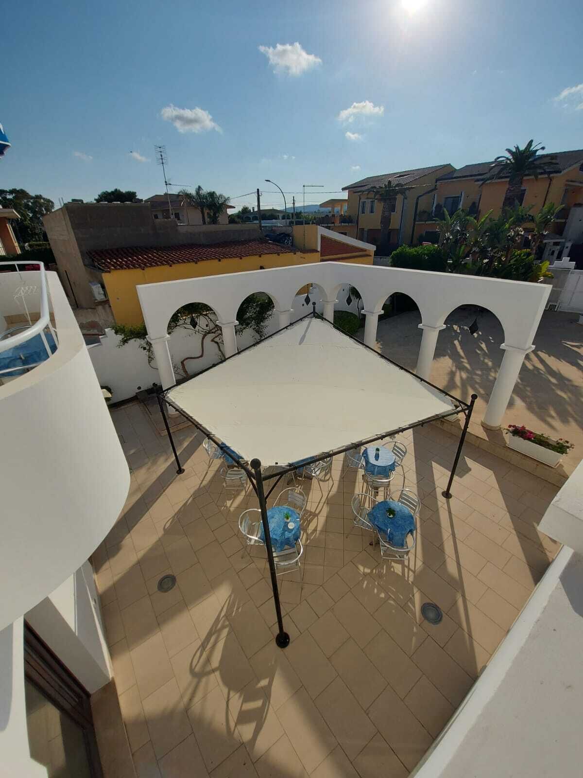 Una terraza en la azotea con una mesa y sillas blancas, rodeada de muros blancos con arcos.