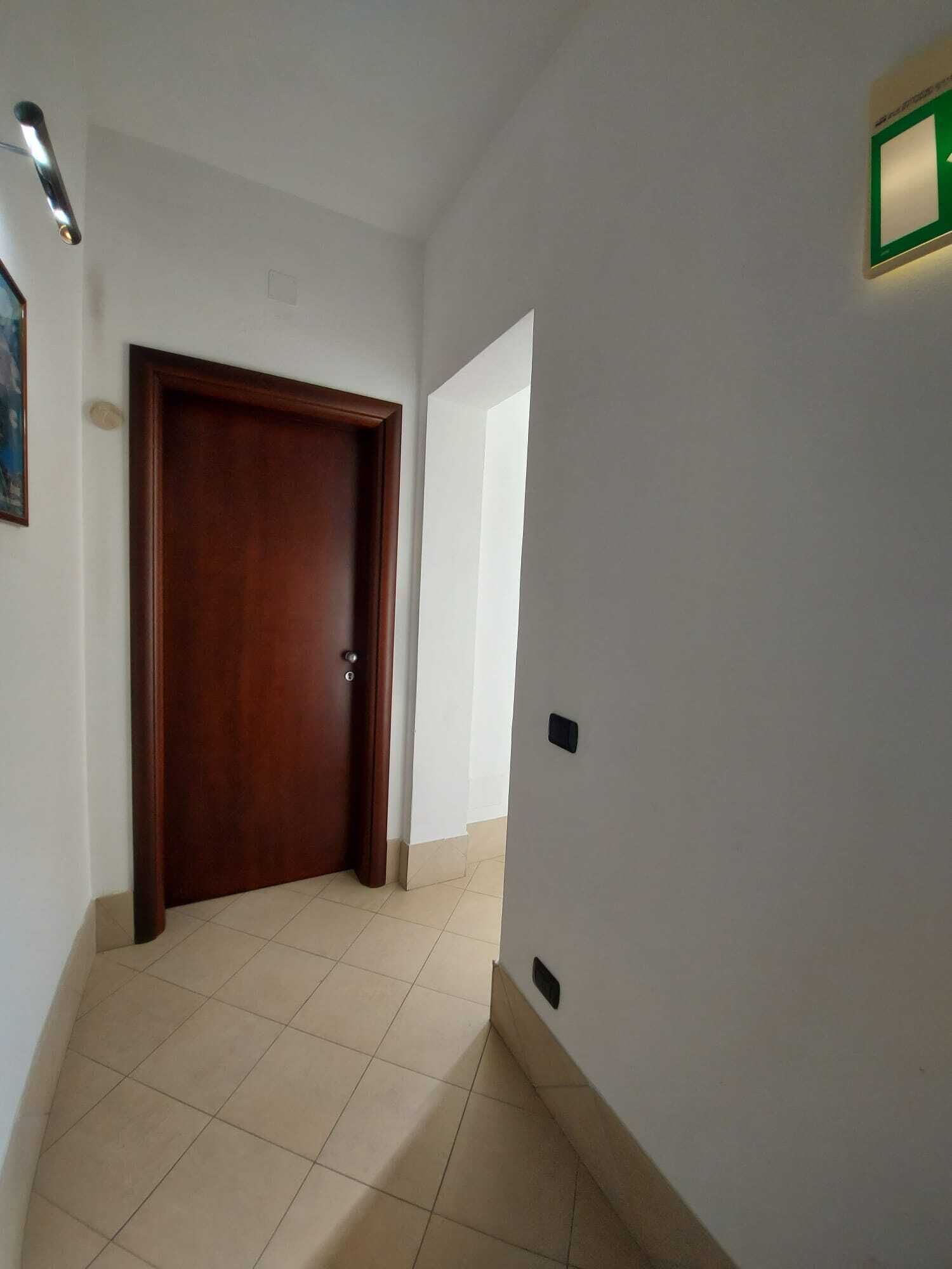 A hallway with a wooden door, white walls, and a tiled floor.