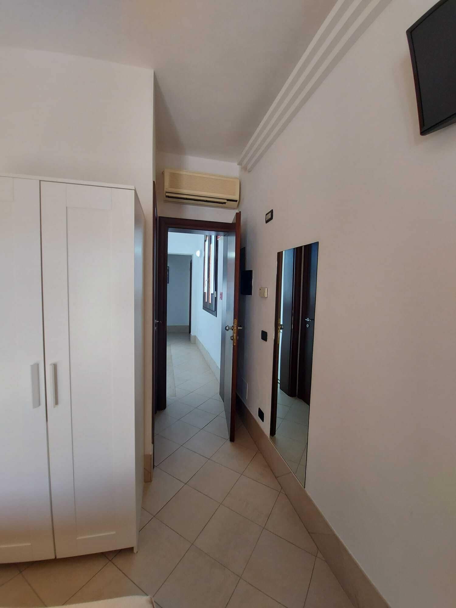 A hallway with a white wardrobe, a door with a mirror, and a wall-mounted air conditioning unit.