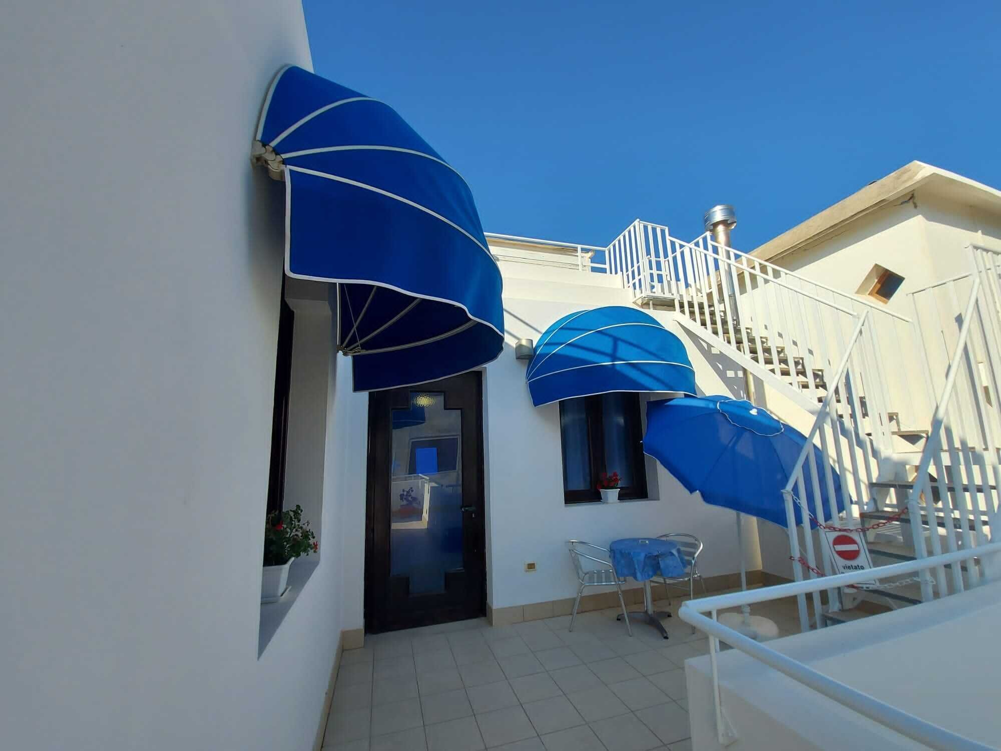 A building with a white exterior, a staircase, and blue umbrellas.