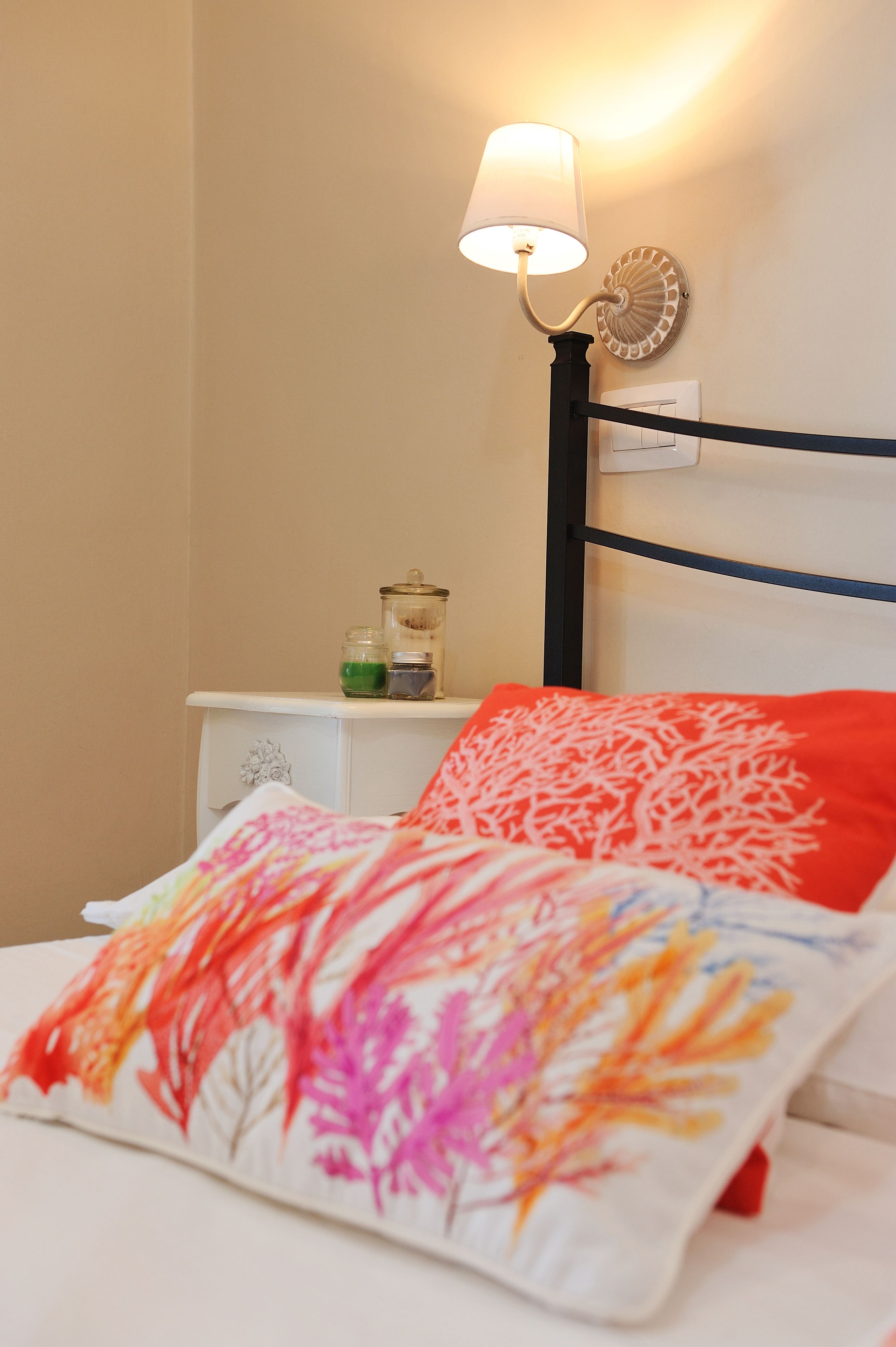 A bed with colorful floral bedding, a bedside lamp, and a small nightstand with jars.