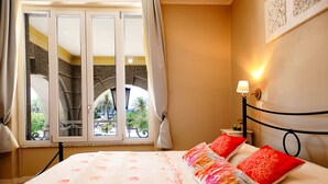 Een hotelkamer met een bed, nachtkastje, lamp en uitzicht op een balkon met buitenmeubilair.